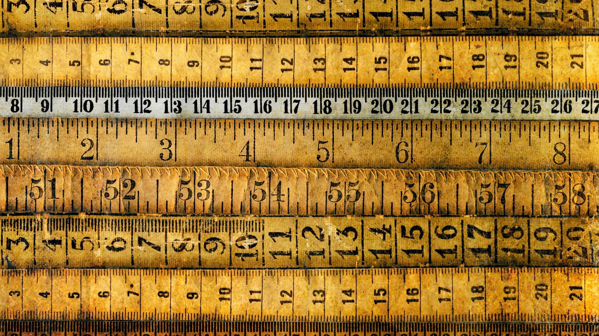Close-up overhead texture of stacked vintage wooden measuring rulers with distinct millimeter and inch graduations.