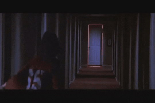 Film still showing an elongated perspective down a dim domestic corridor with an open doorway at the far end, demonstrating optical expansion.