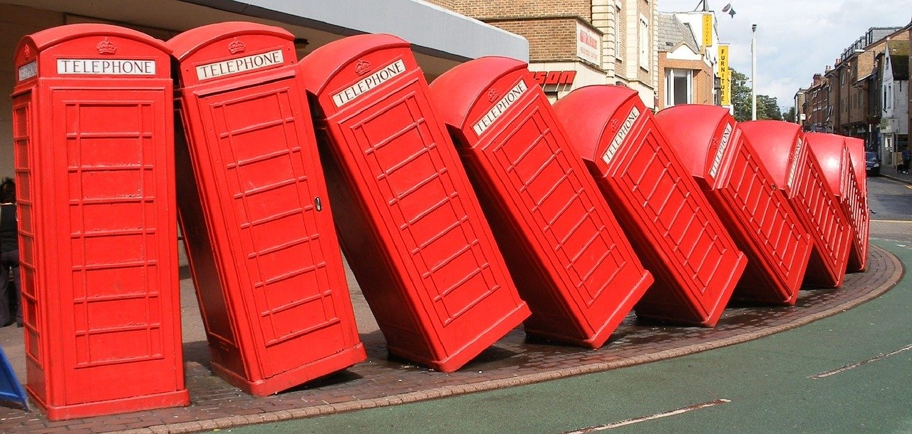 Sculpture of classic red British telephone boxes falling like dominoes in a curved row along a street pavement.