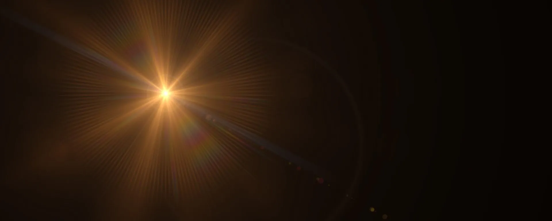 Bright golden optical lens flare radiating light against a pitch-black background.
