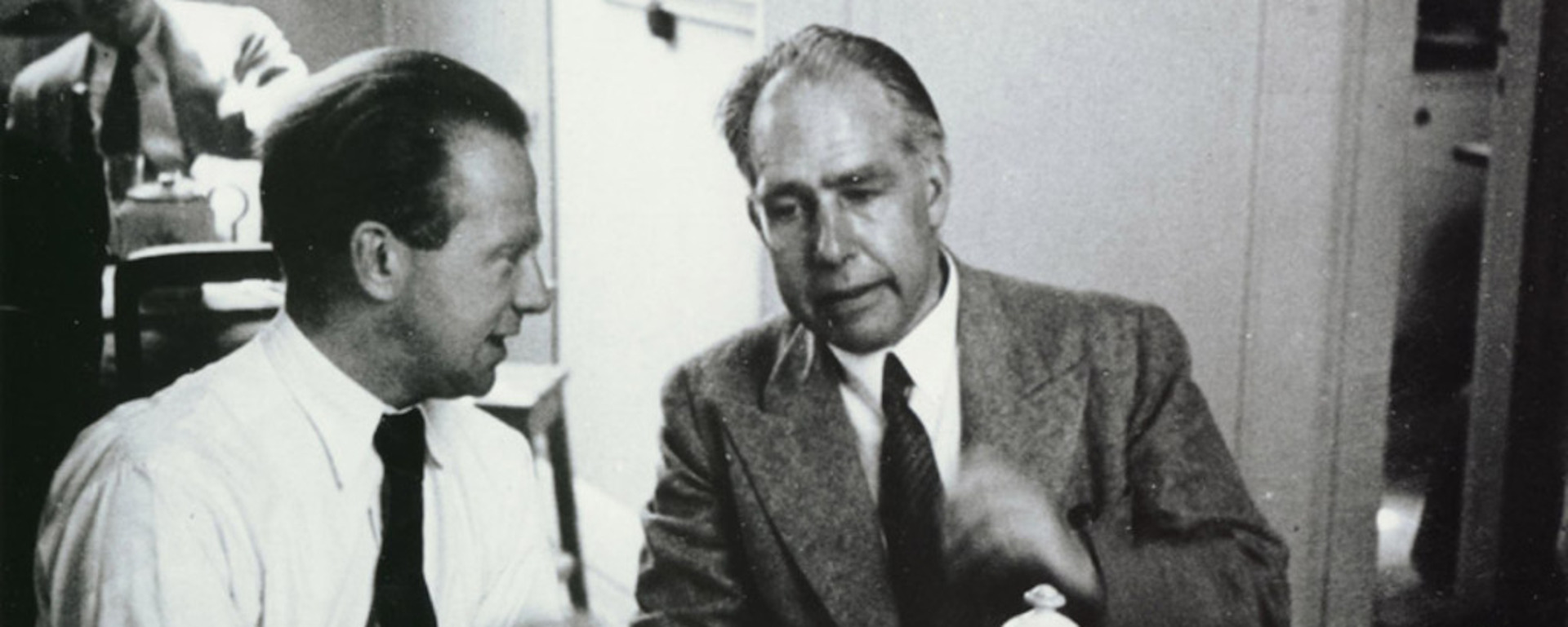 Archival black and white photograph of physicists Werner Heisenberg on the left and Niels Bohr on the right engaged in discussion at a table.