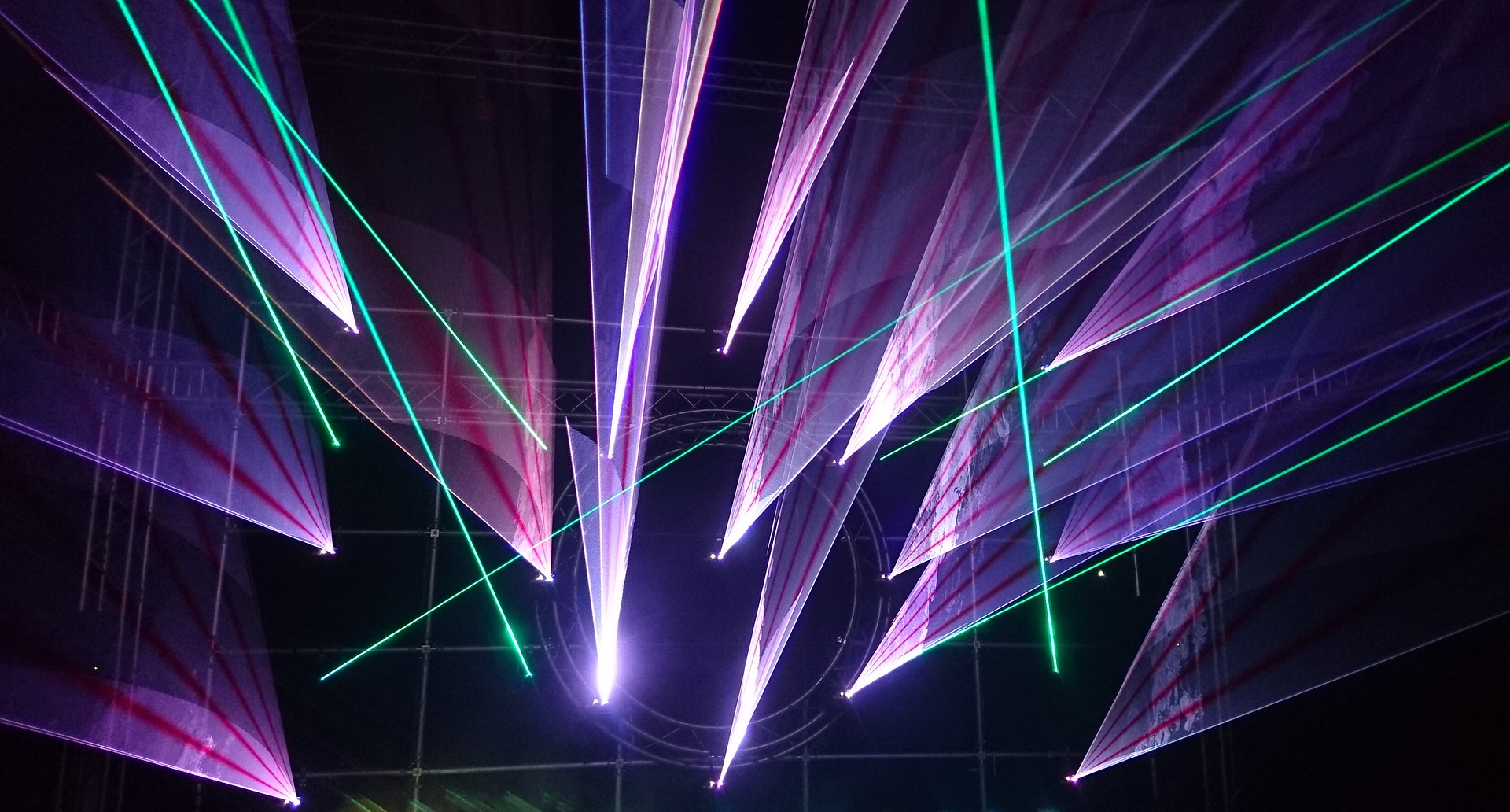 Laser light show displaying geometric cones and planes of purple and bright green light projecting into a dark arena.